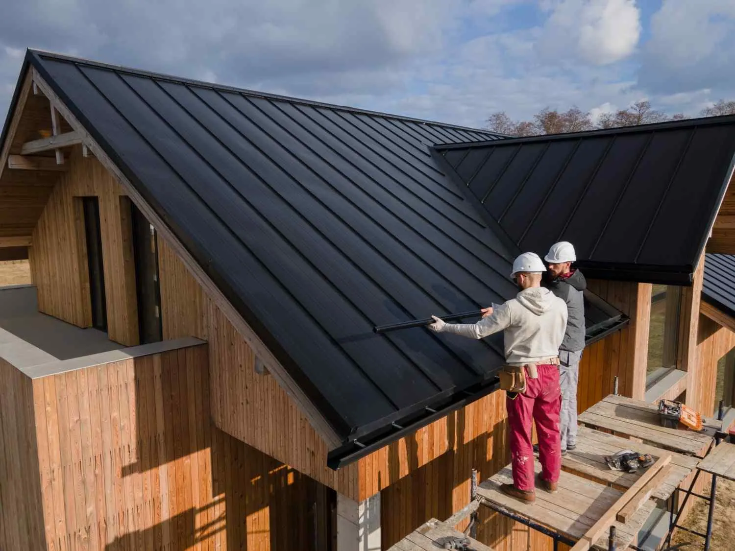 Two roofers looking over the edge of a dark metal roof on a timber house